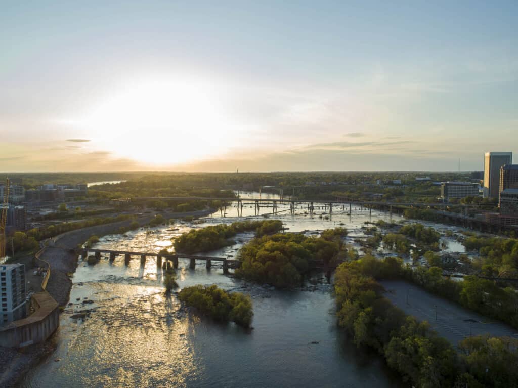 Aerial view of downtown Richmond, Virginia at sunset with the James River, bridges, and tree-covered islands.